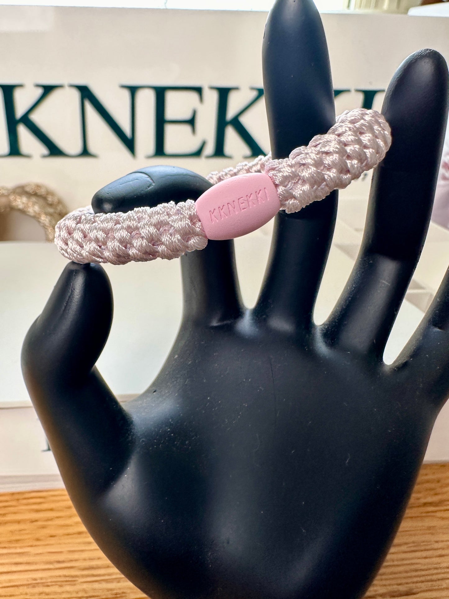 KKNEKKI Ballet Pink hair elastic shown on a model black hand in front of a KKNEKKI Box