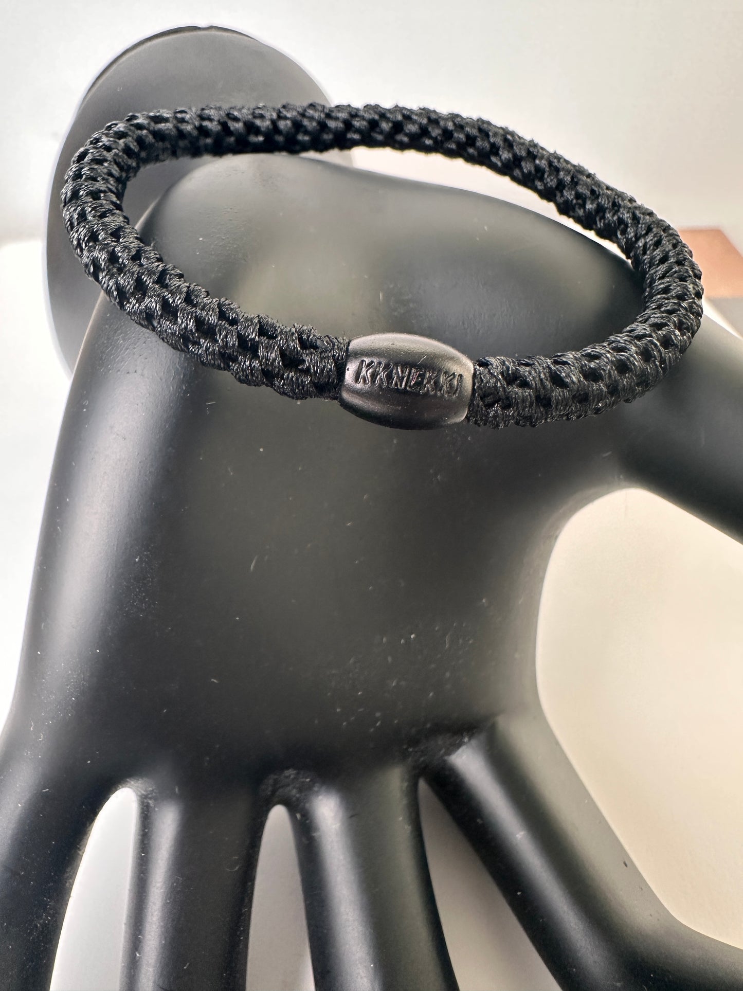 KKNEKKI Black Slim hair tie on black model hand and white background