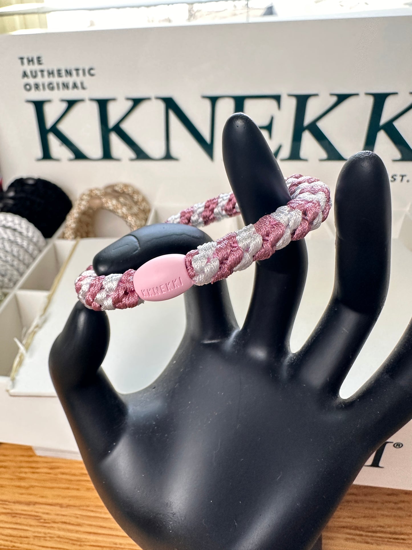 KKNEKKI Old Pink & White Stripe hair elastic on a black model hand with KKNEKKI Box and more hair ties in the background