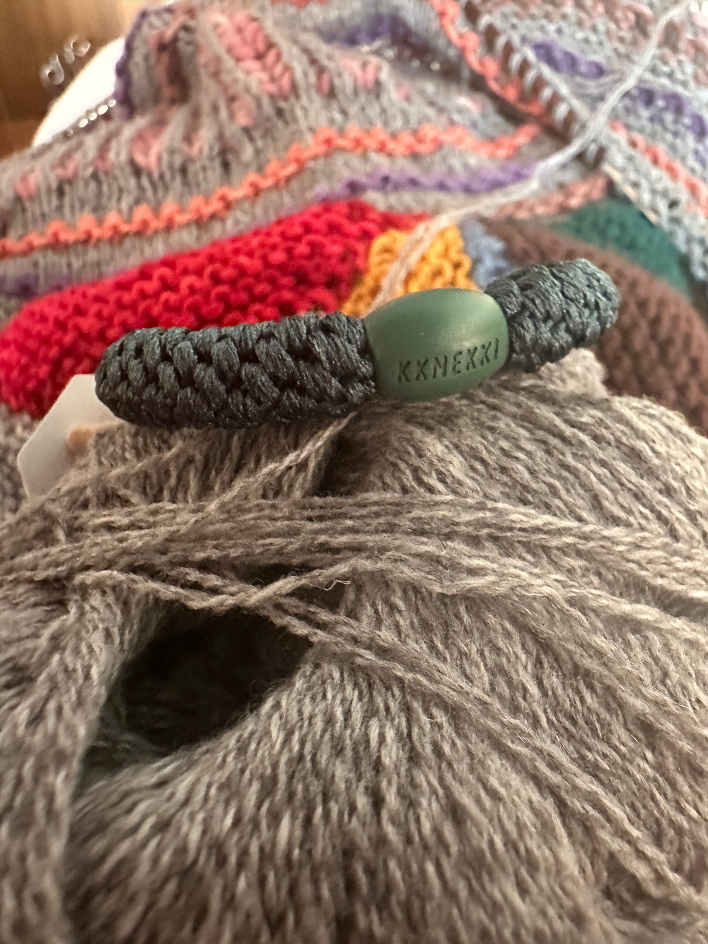 KKNEKKI Peacock hair elastic atop a pile of knitting and yarn show it's rich color and branded bead
