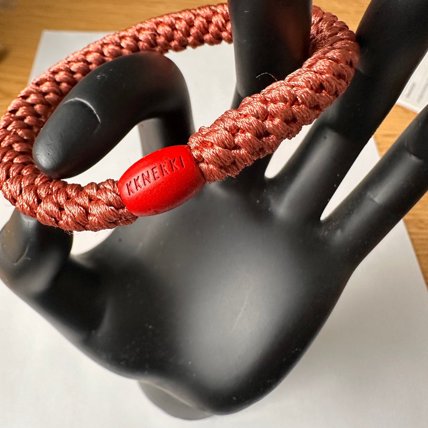 KKNEKKI Terracotta hair elastic shown on black model hand with branded bead clearly shown