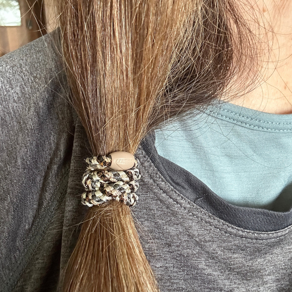 A close-up of a person's hair tied in a low ponytail with a woven KKNEKKI  hair elastic in Slim Mix Copper Grey Glitter.