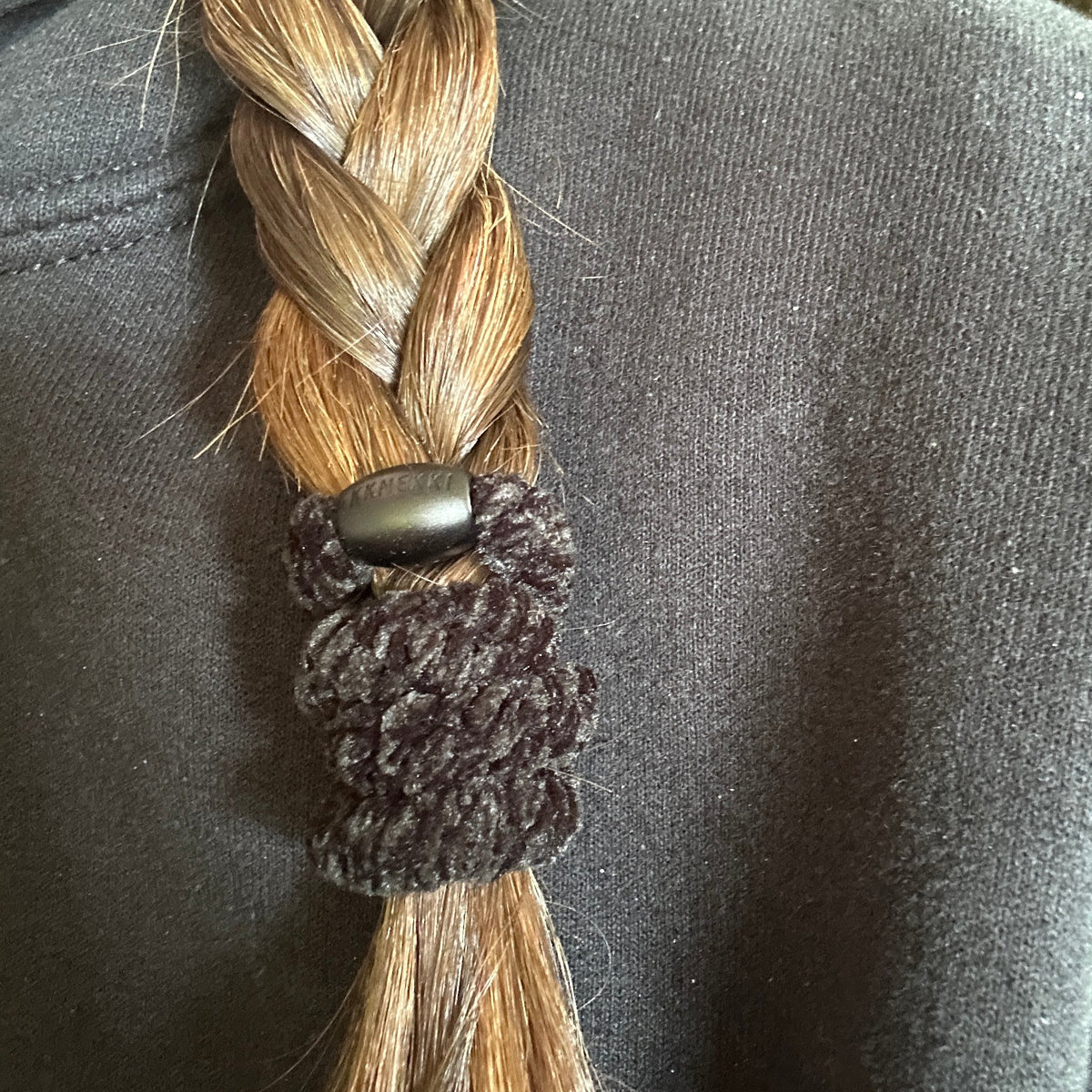 A close-up of a person's light brown hair tied in a braid with a KKNEKKI hair elastic in the color Black Velvet, worn over a black hoodie.