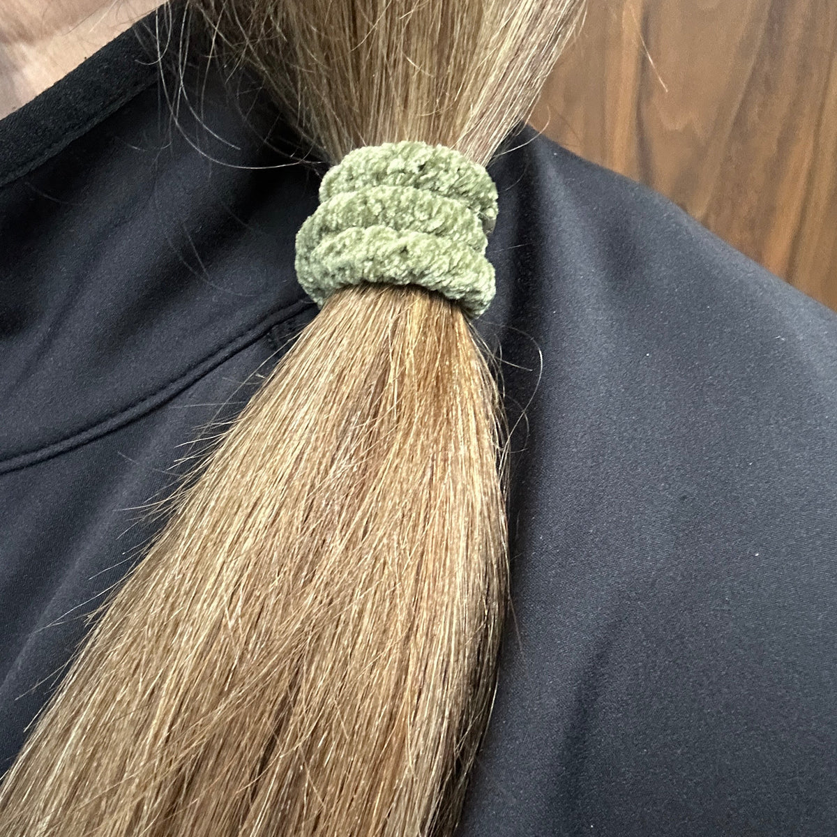 A close-up of a person's light brown hair tied in a side ponytail  with a KKNEKKI hair elastic in the Moss (green) Velvet, worn over a black jacket.