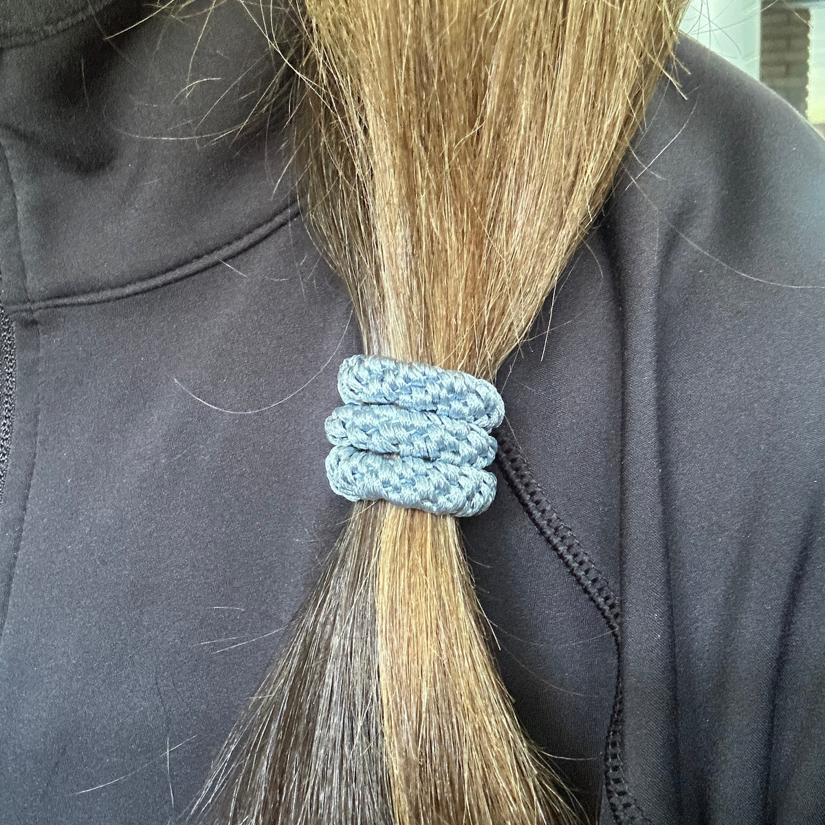 A close-up of a person's long light brown hair tied back with an authentic original KKNEKKI  hair tie in Sea Blue color, wearing a black athletic top.