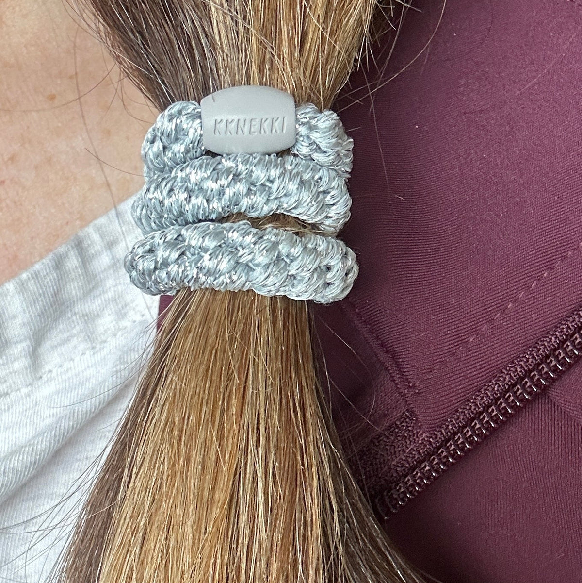 A close up of KKNEKKI Silver Glitter hair elastic on woman's brown ponytail