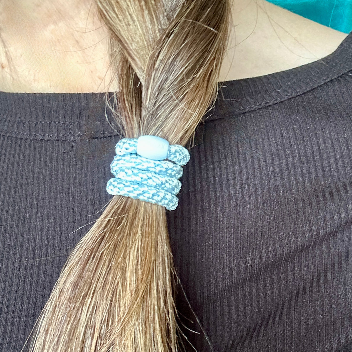 Close-up of a person's hair tied in a low braid with a KKNEKKI Slim Baby Blue light blue hair elastic over dark ribbed top