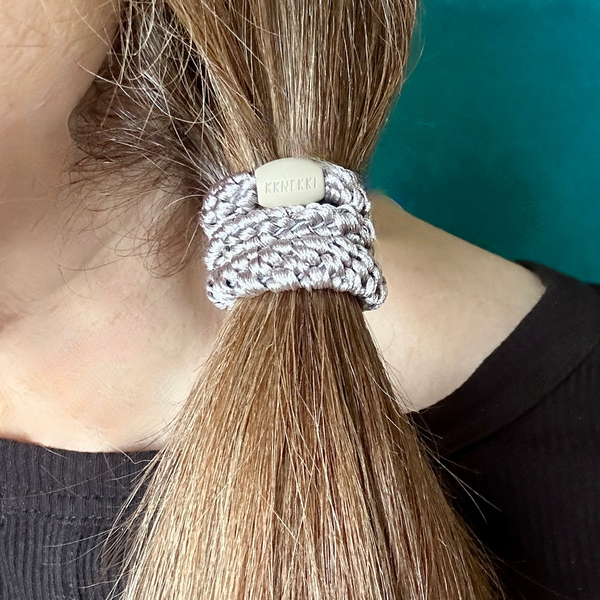 Close up of a person's brown hair secured in a ponytail with a KKNEKKI Light Mole colored hair elastic, branded bead visible