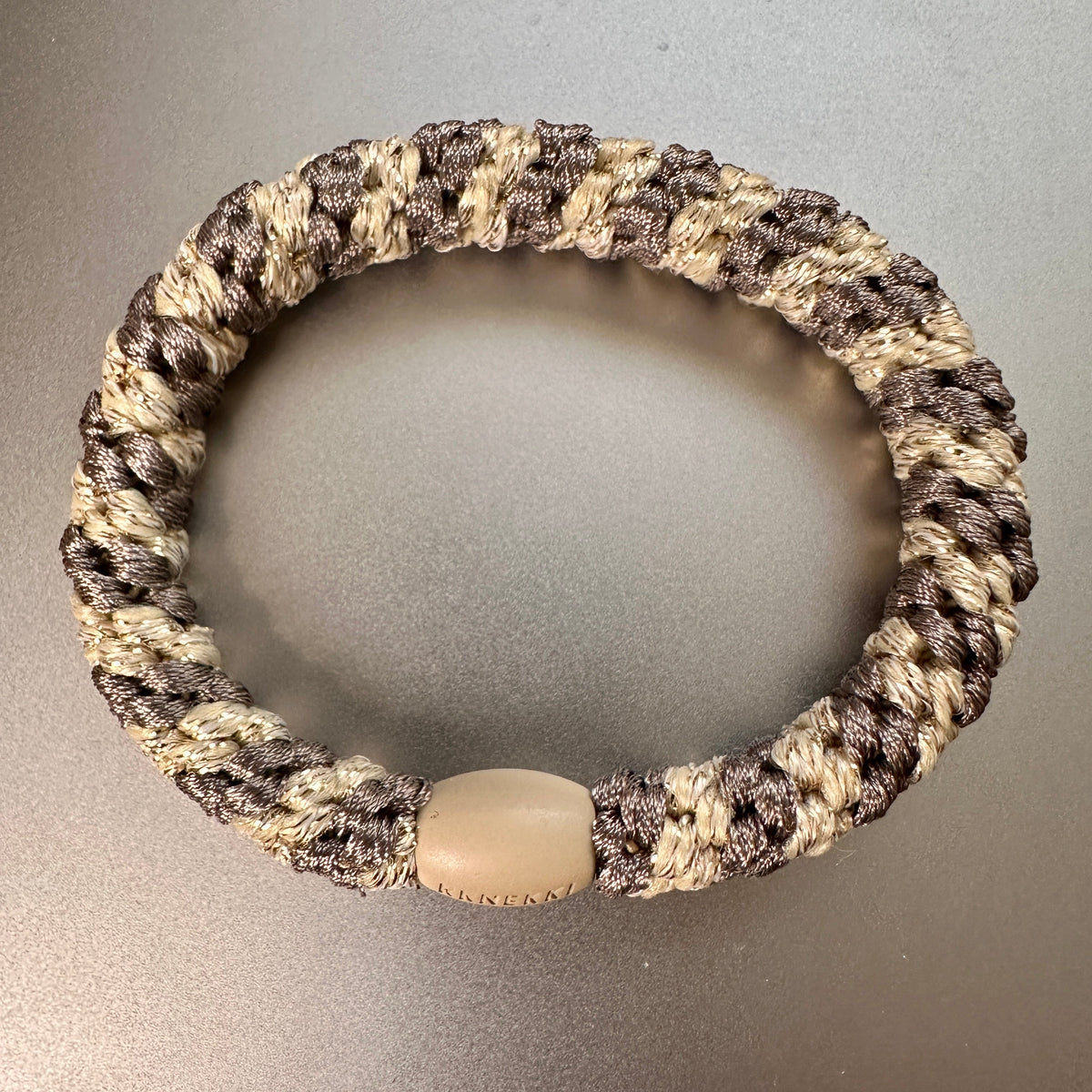 IKKNEKKI Mole Beige Glitter Stripe 60 Plus woven strand hair elastic on silver background