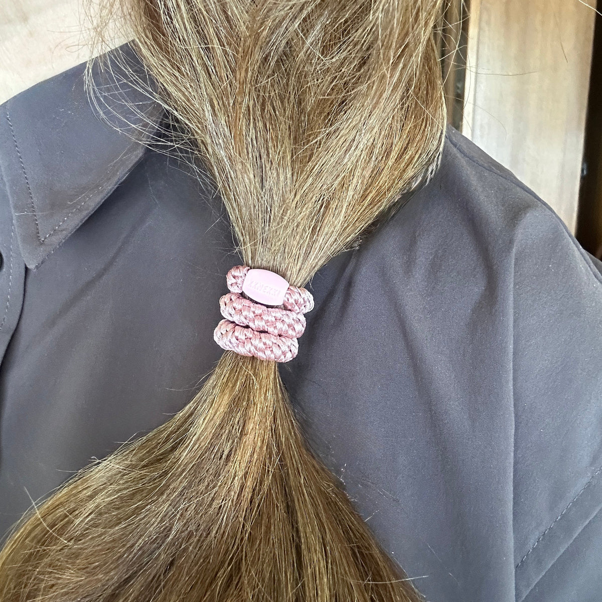 KKENKKI Dusty Rose colored hair elastic on person's ponytail in front of dark brown shirt
