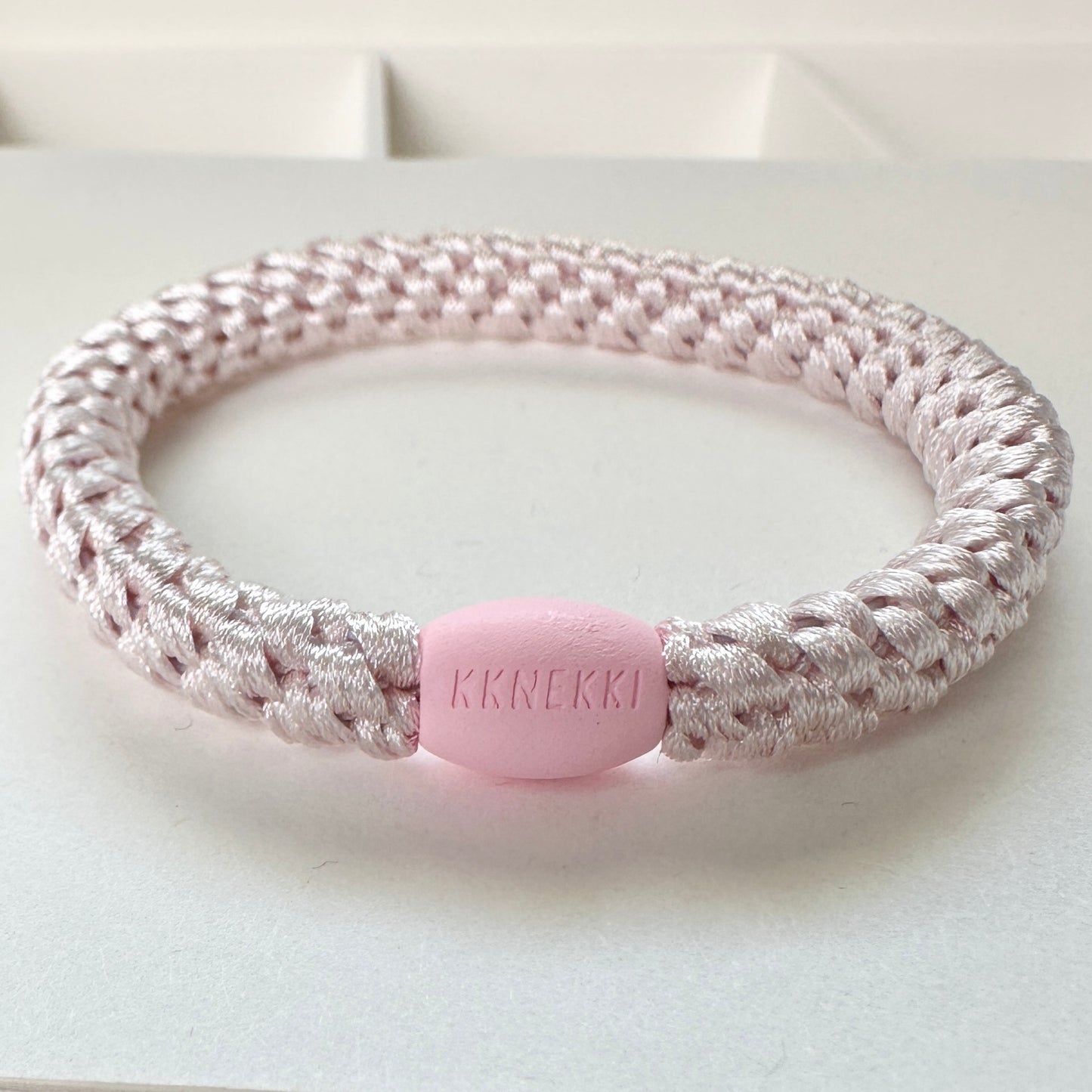 KKNEKKI Ballet Pink hair elastic shown slightly on its side with branded bead visible sitting on a white background.