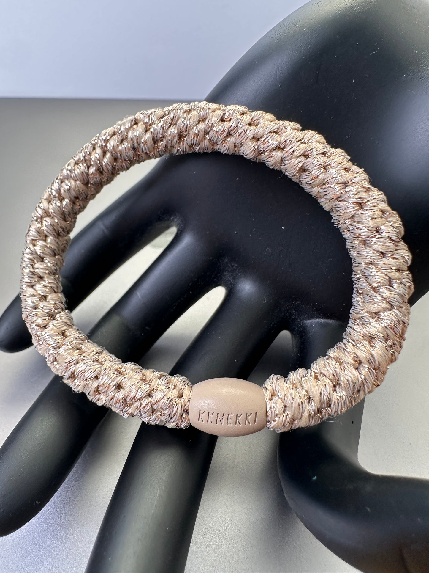 KKNEKKI Beige Glitter hair elastic on black model hand with branded bead visible