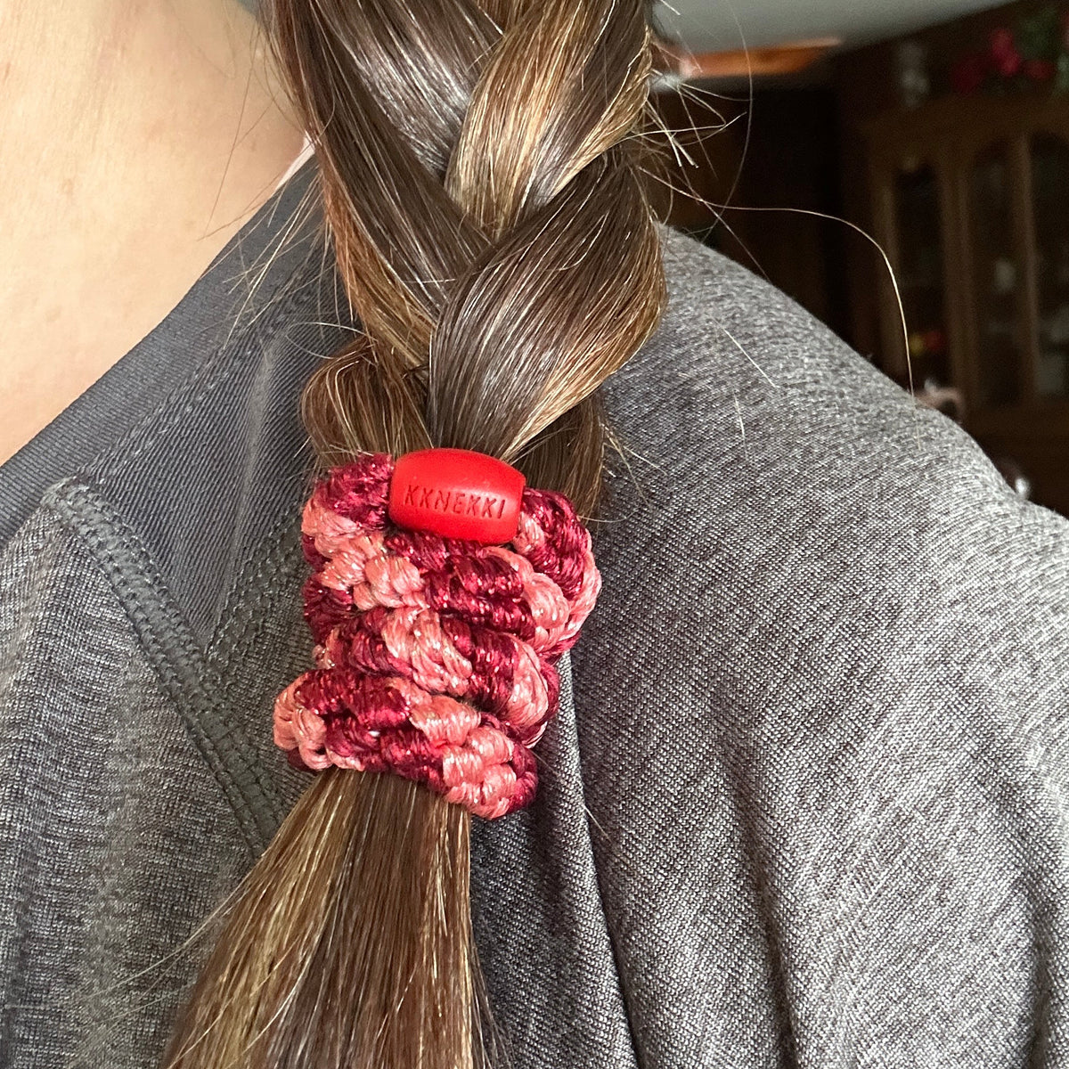 KKNEKKI Coral Bordeaux Glitter Stripe hair elastic in braided brown hair, branded bead visible