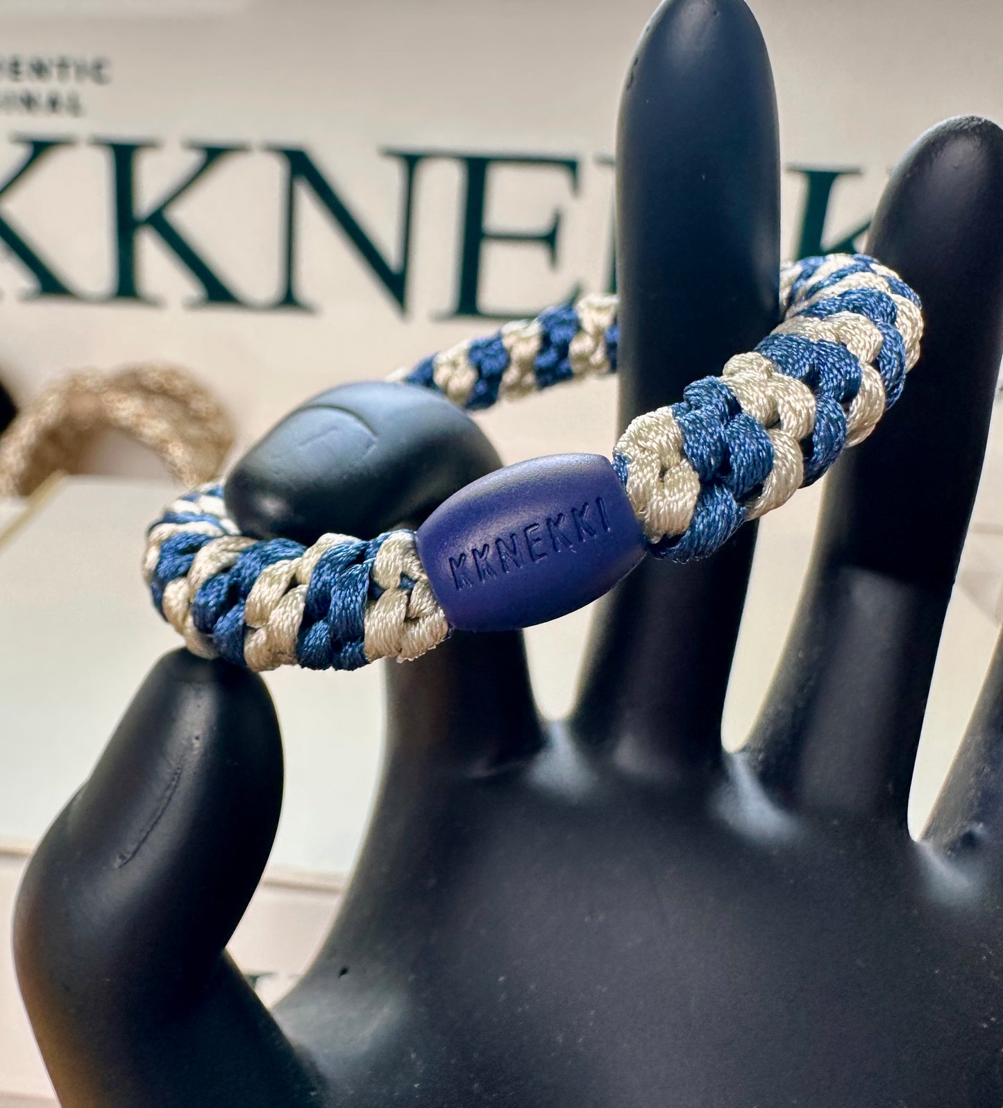 KKNEKKI Indigo Ivory Stripe hair elastic on black hand model showing branded bead in front of KKNEKKI sign