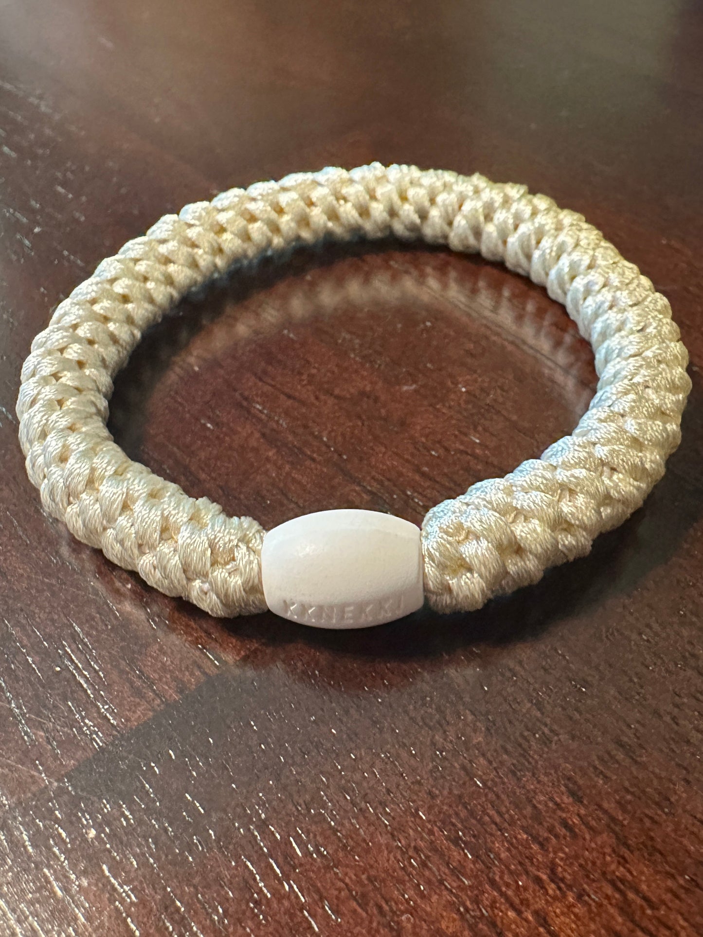 KKNEKKI Ivory hair tie on brown table branded bead seen