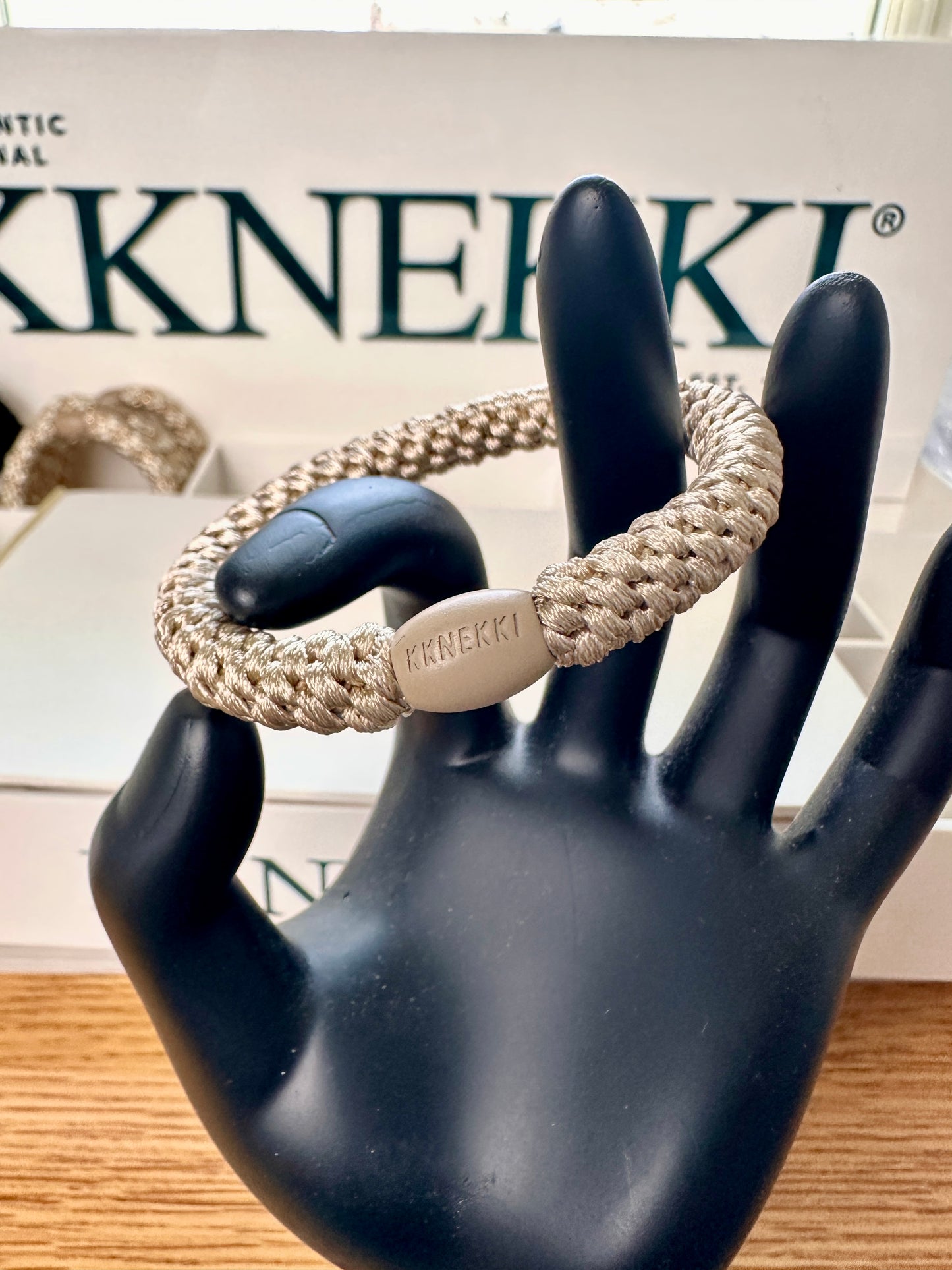 KKNEKKI Light Beige hair elastic on black model hand in front of a KKNEKKI branded box