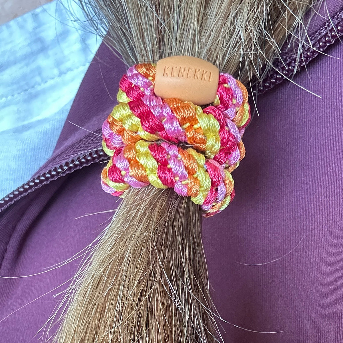 KKNEKKI Mix Sun-Orange striped hair elastic on woman's braid, branded bead visible