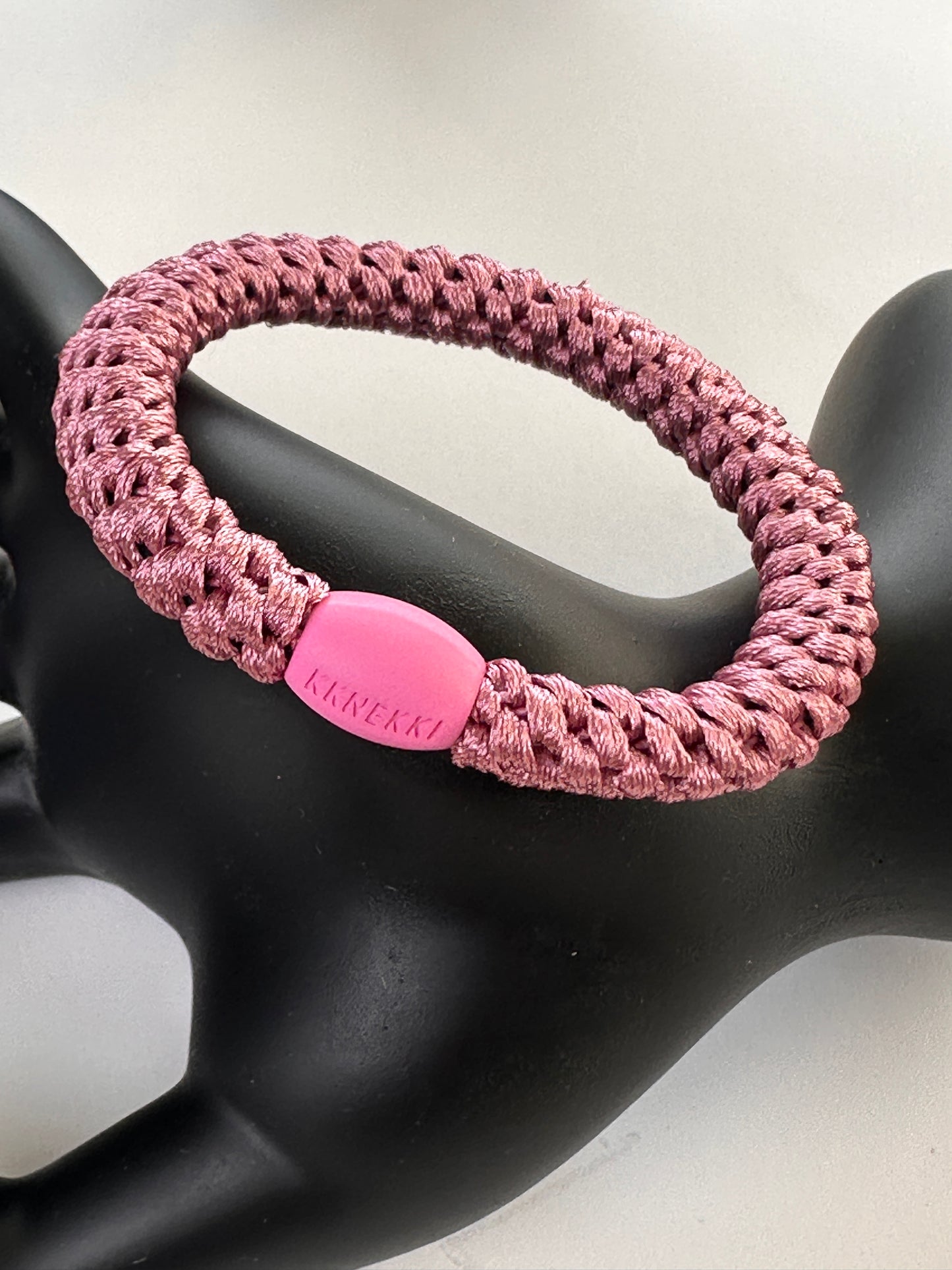 KKNEKKI Old Pink hair elastic on black model hand in front of white background