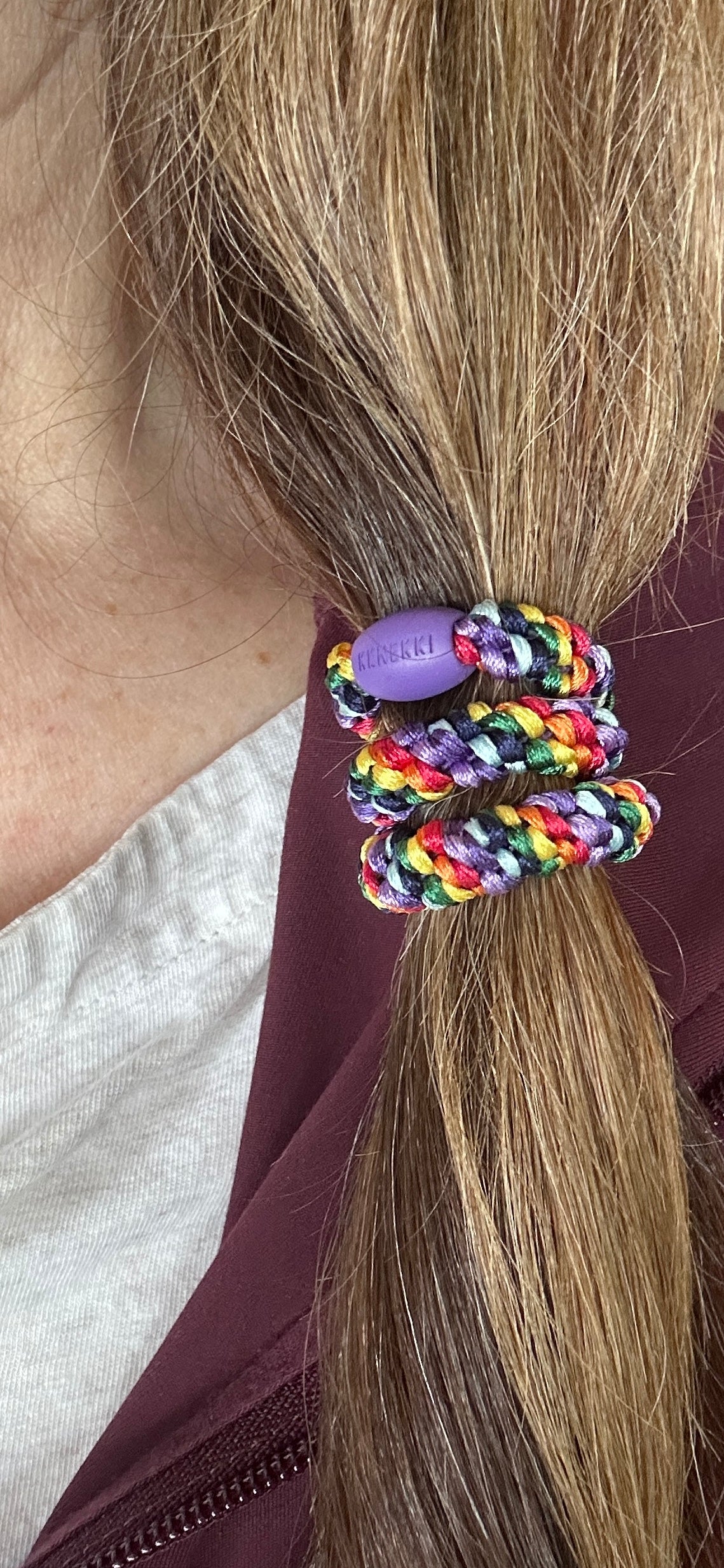 KKNEKKI Rainbow hair tie in woman's brown hair against a maroon jacket and white tank