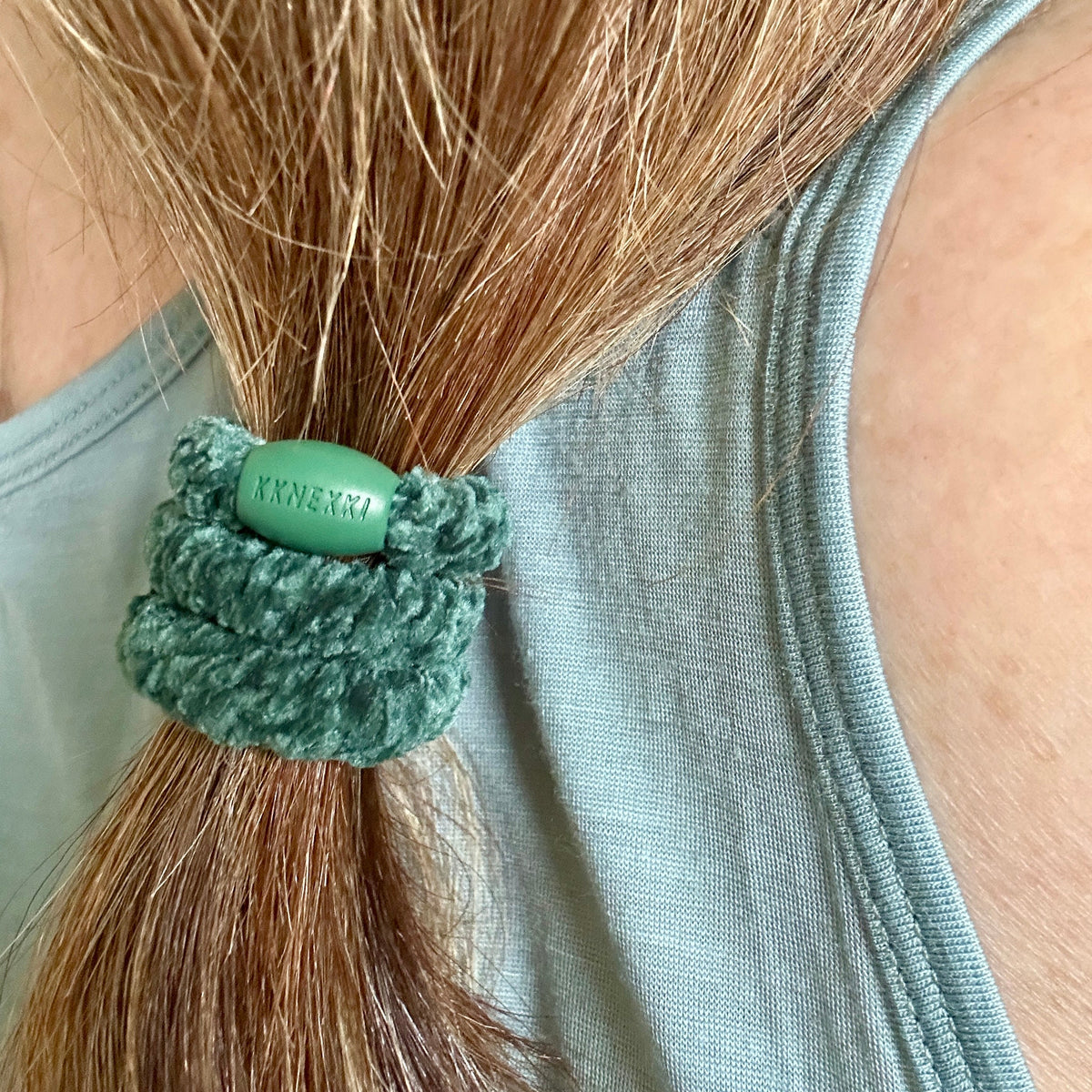 KKNEKKI Velvet Green hair elastic in woman's brown hair ponytail, branded bead visible